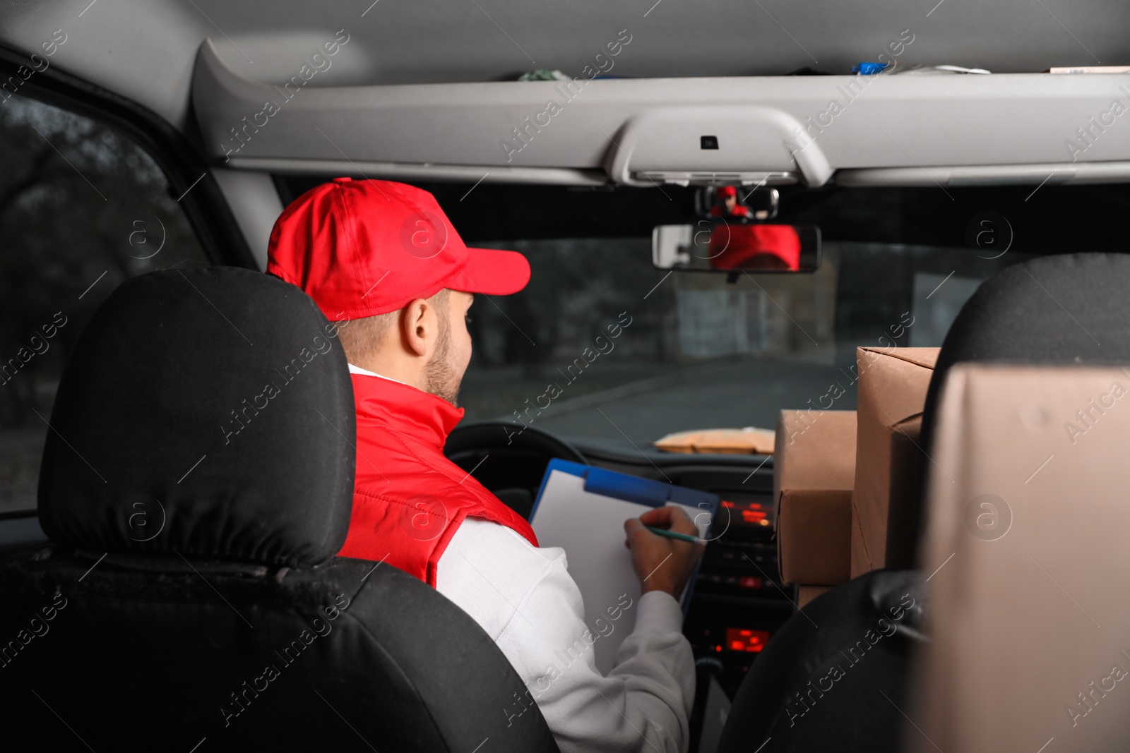 Photo of Deliveryman with clipboard and parcels in car