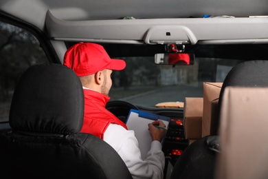 Photo of Deliveryman with clipboard and parcels in car