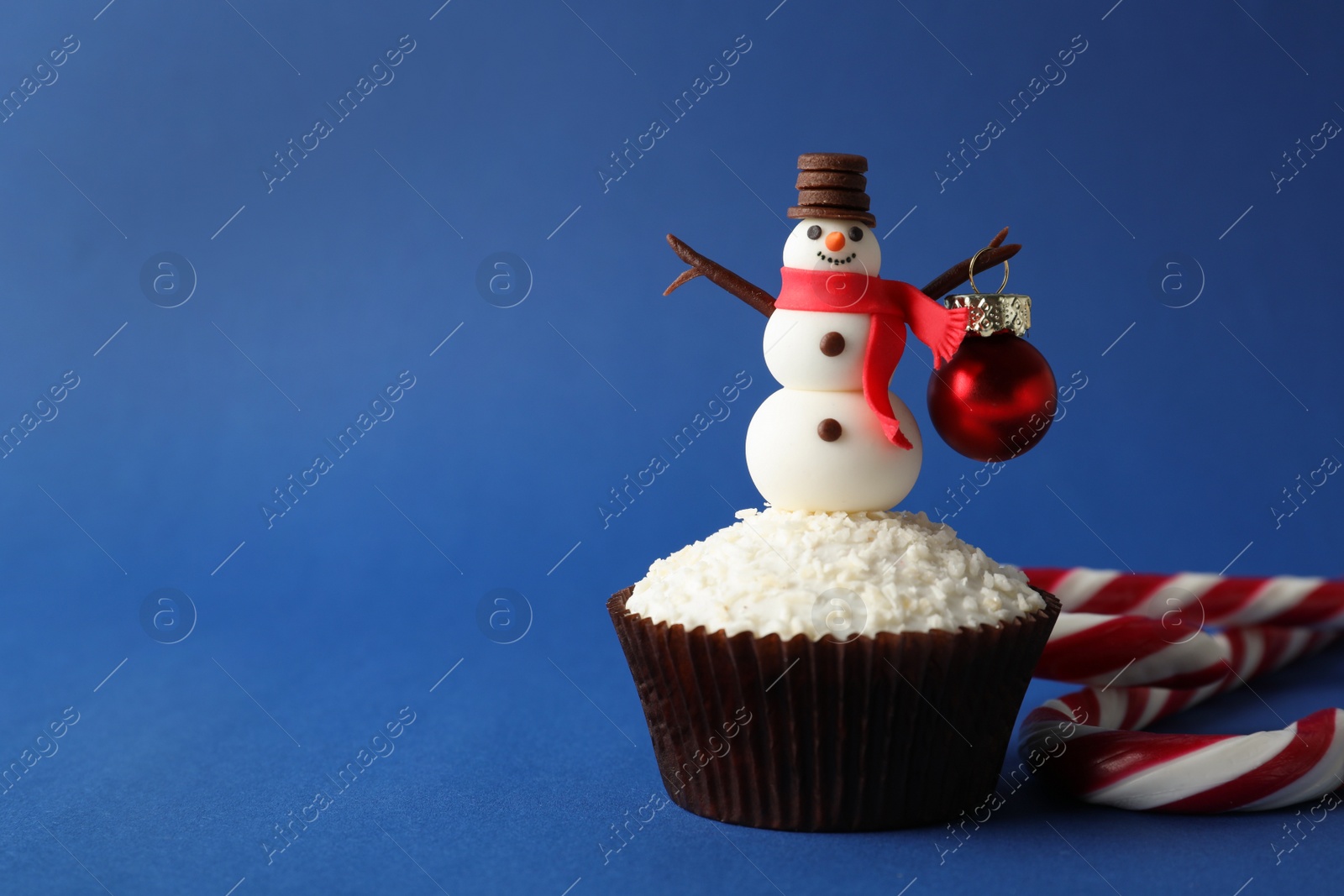 Photo of Tasty cupcake with snowman figure and Christmas bauble on blue background, space for text