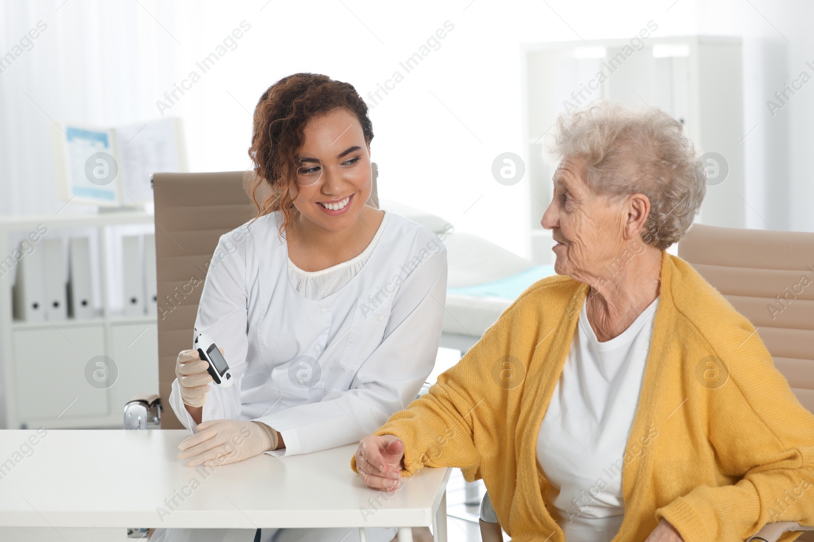 Photo of Doctor checking patient's blood sugar level with digital glucometer at table. Diabetes control