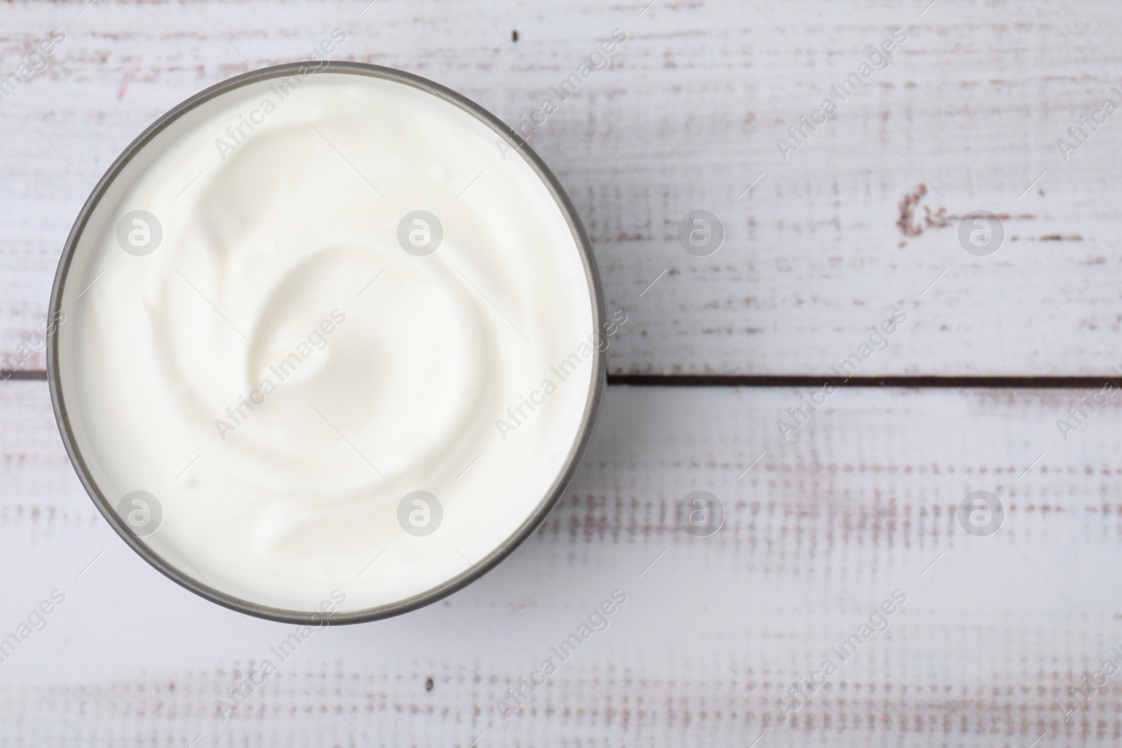 Photo of Delicious natural yogurt in bowl on light wooden table, top view. Space for text