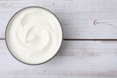 Delicious natural yogurt in bowl on light wooden table, top view. Space for text