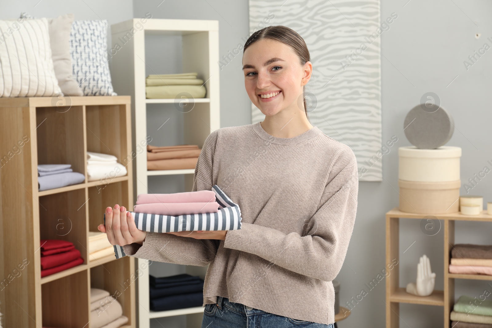 Photo of Smiling young woman with stack of bed linens in shop