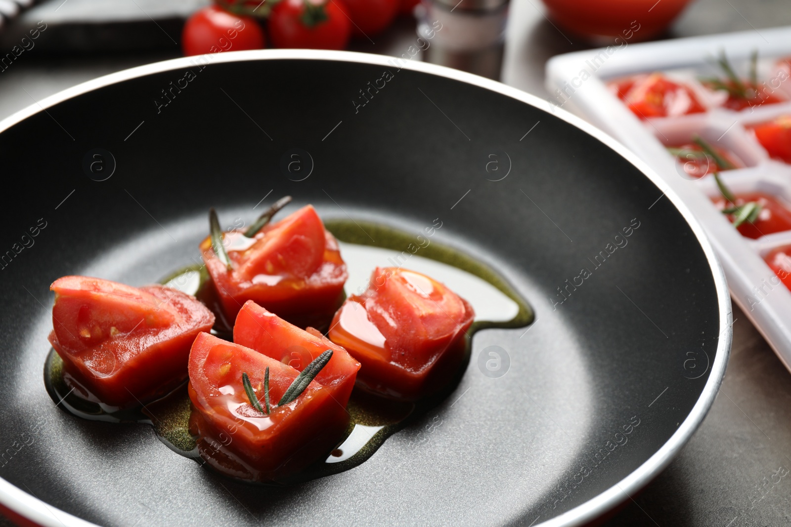 Photo of Melting ice cubes with tomatoes, oil and rosemary on grey table, closeup