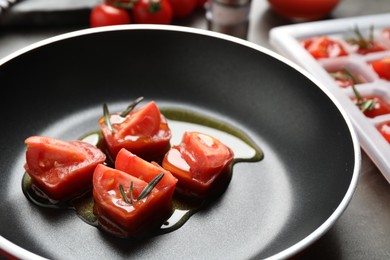 Photo of Melting ice cubes with tomatoes, oil and rosemary on grey table, closeup