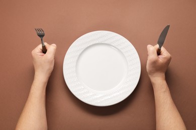 Photo of Man with cutlery and empty plate at brown table, top view
