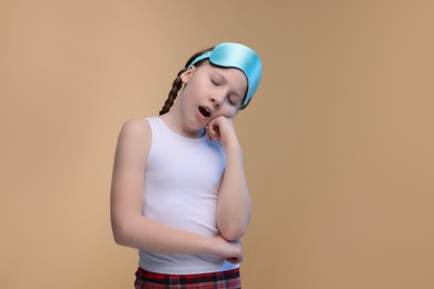 Photo of Girl with sleep mask yawning on beige background. Insomnia problem