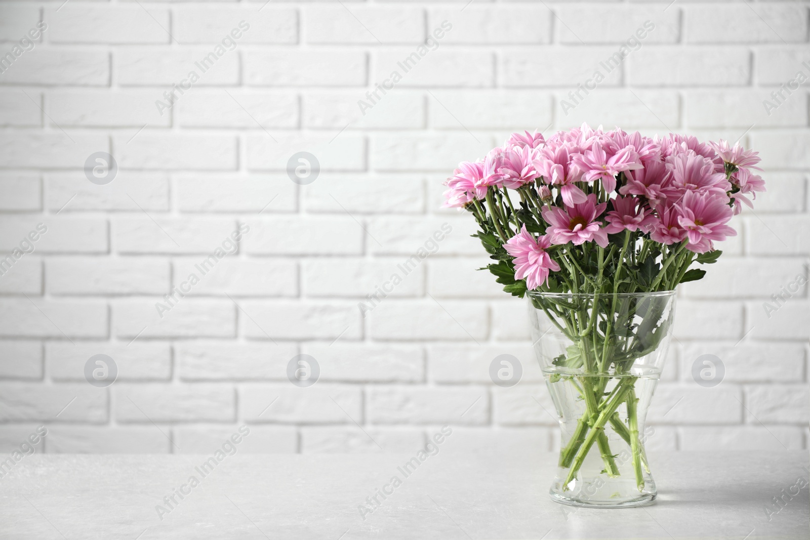 Photo of Vase with beautiful chamomile flowers on grey table against white brick wall. Space for text
