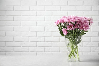 Vase with beautiful chamomile flowers on grey table against white brick wall. Space for text