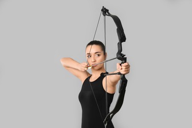 Young woman practicing archery on light grey background