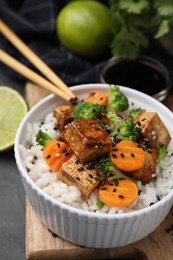 Photo of Bowl of rice with fried tofu, broccoli and carrots on grey wooden table, closeup