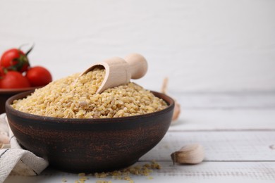 Photo of Bowl and scoop with raw bulgur on white wooden table, closeup. Space for text