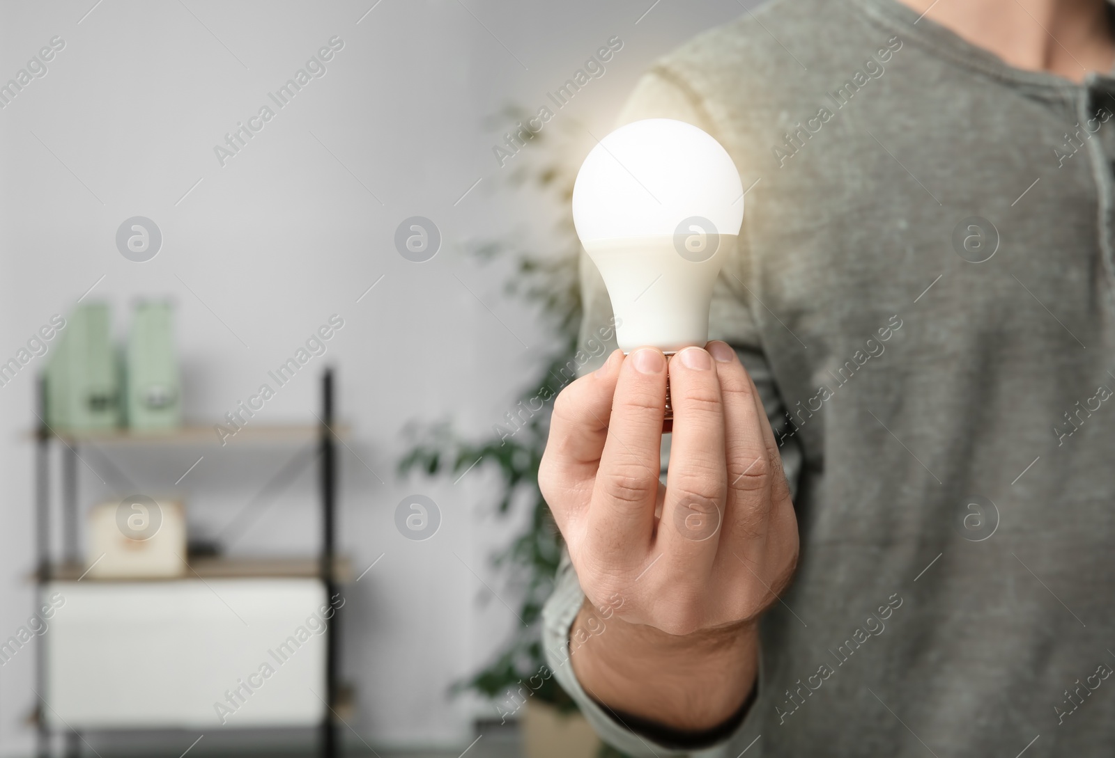Photo of Man holding lamp bulb on blurred background, closeup with space for text