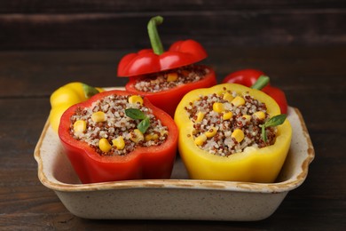 Photo of Quinoa stuffed bell peppers and basil in baking dish on wooden table, closeup