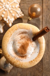 Photo of Tasty eggnog with cinnamon, cookies and Christmas baubles on wooden table, flat lay