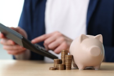 Photo of Financial savings. Man using calculator at wooden table, focus on piggy bank and stacked coins