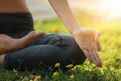 Image of Woman meditating on green grass at sunrise, closeup view. Practicing yoga