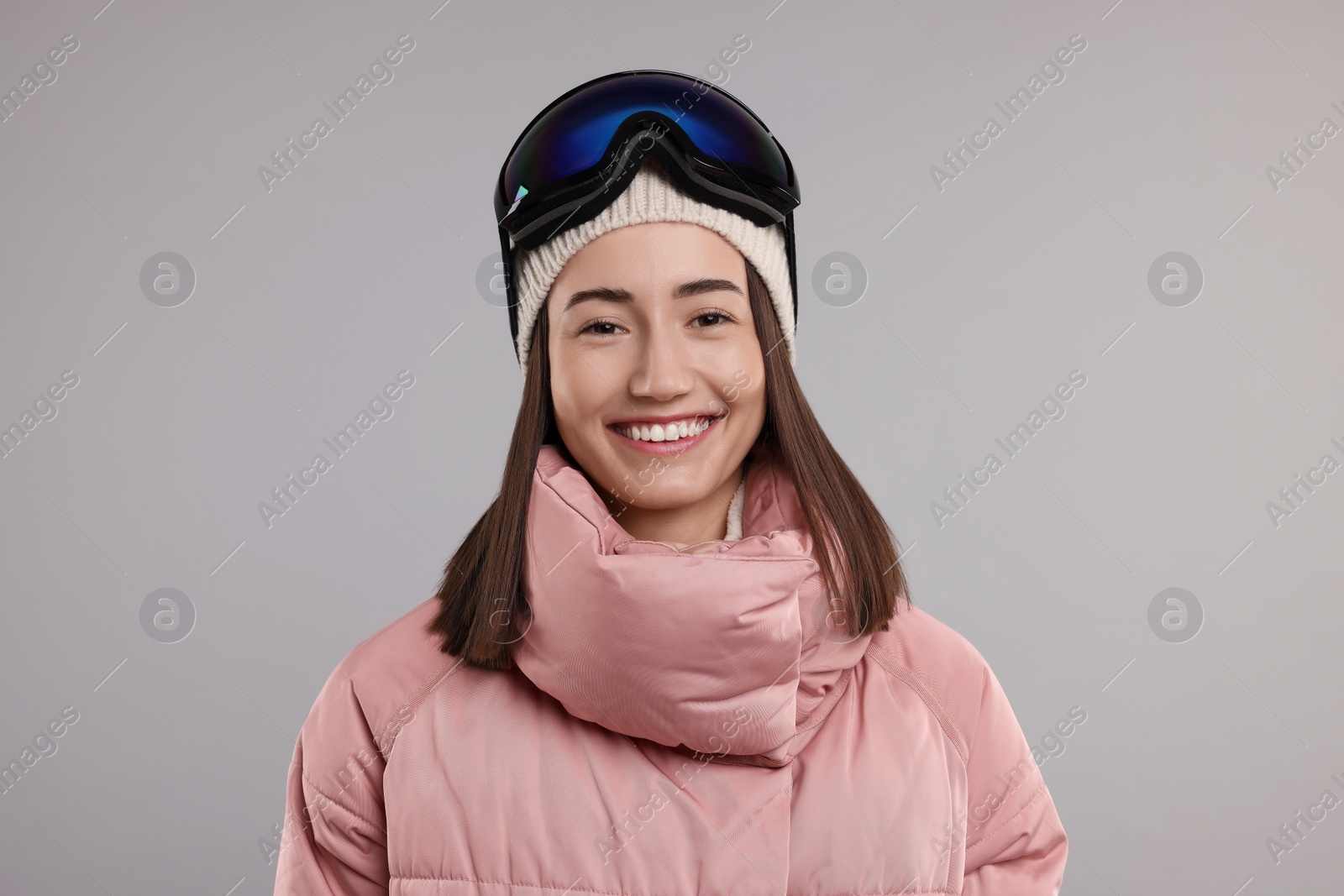 Photo of Winter sports. Happy woman with snowboard goggles on grey background