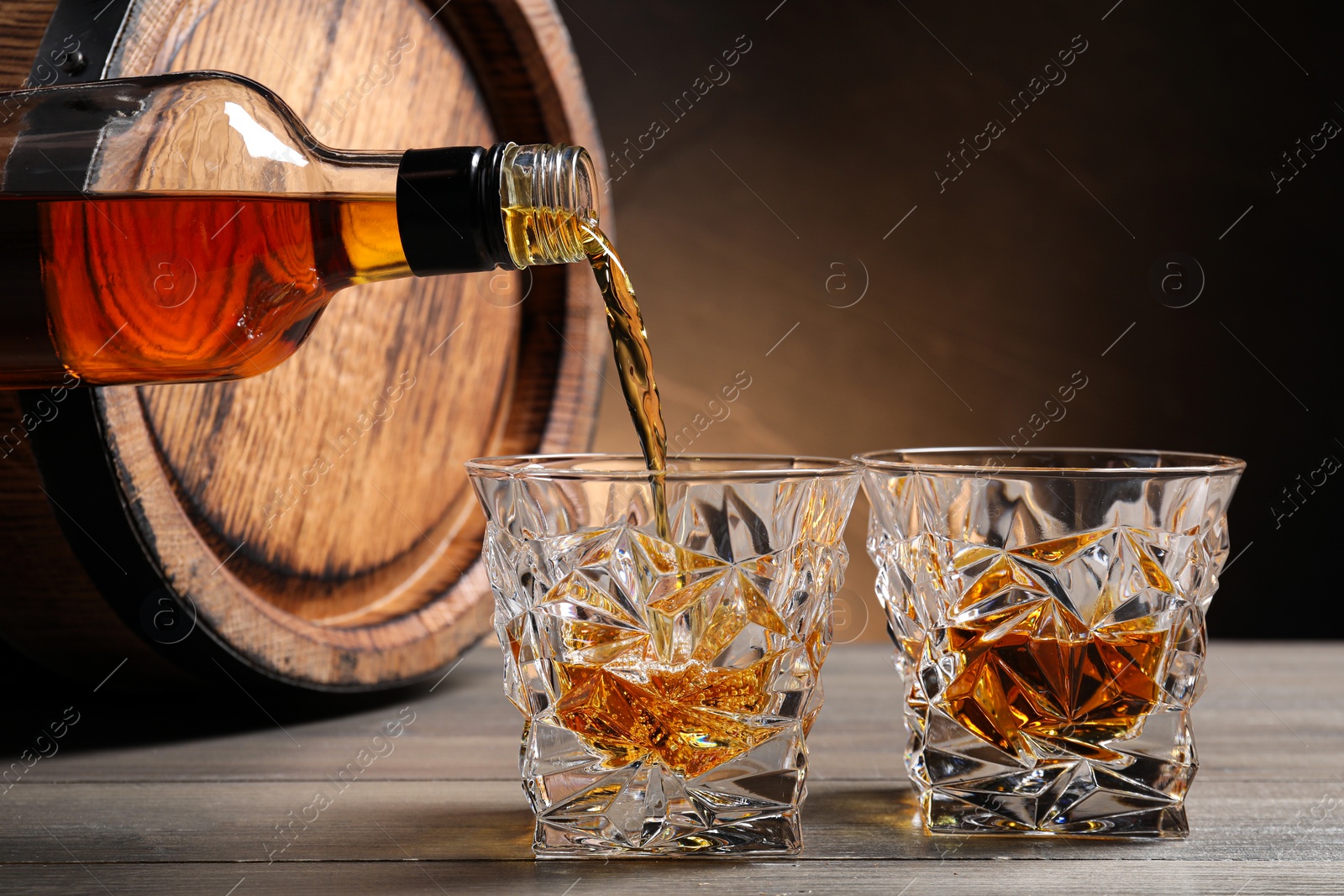 Photo of Pouring whiskey into glass from bottle near wooden barrel on table