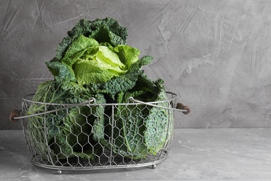 Photo of Fresh green savoy cabbage in basket on marble table against grey background. Space for text