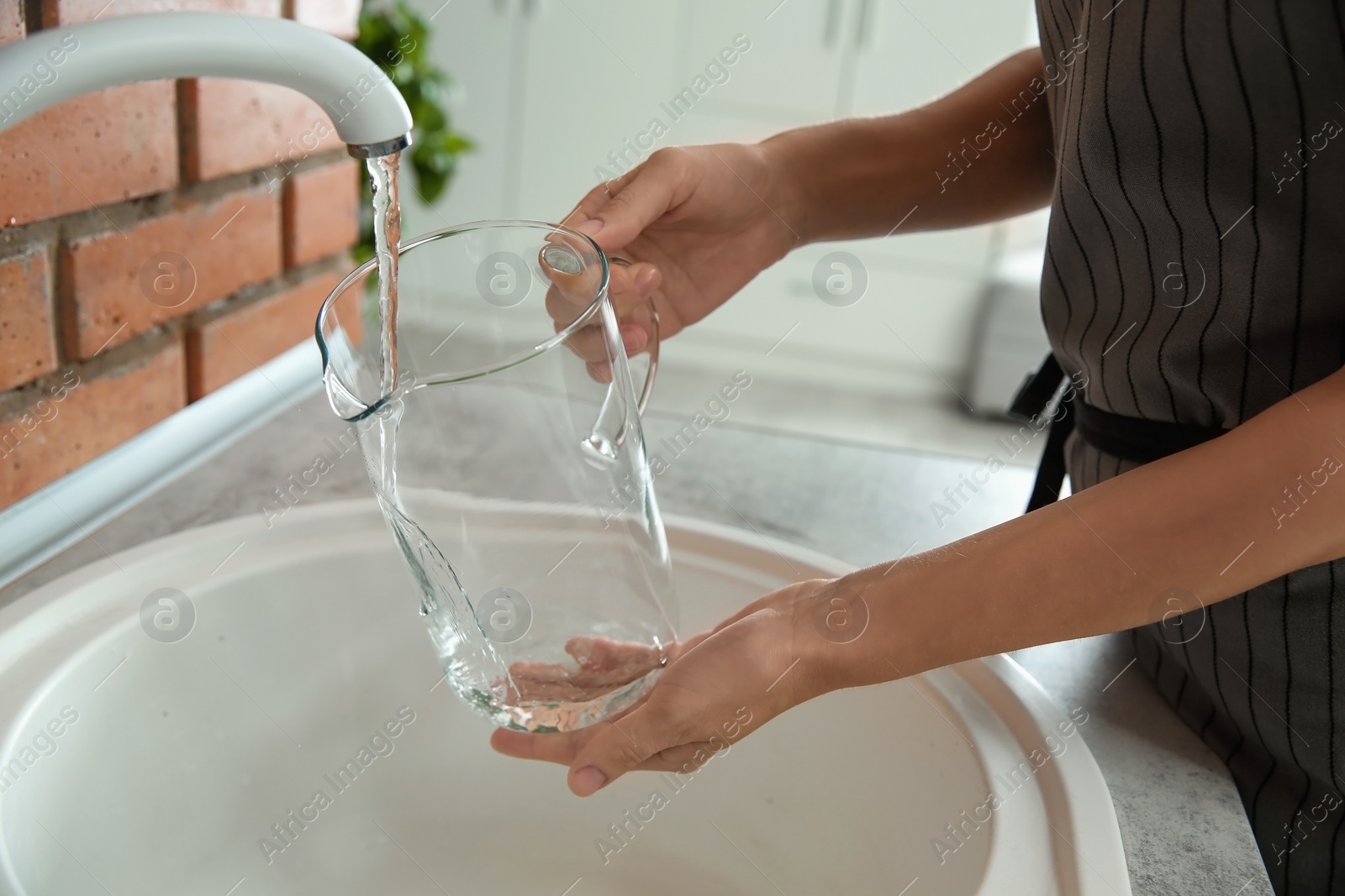 Photo of Woman filling glass pitcher with water, closeup