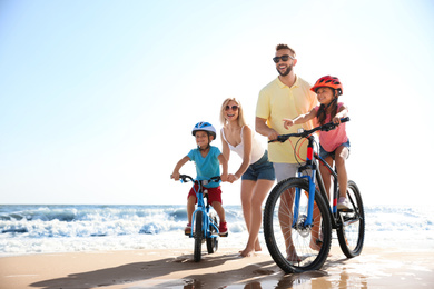 Happy parents teaching children to ride bicycles on sandy beach near sea