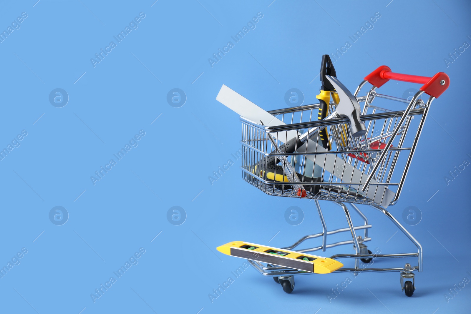 Photo of Small shopping cart with set of construction tools on light blue background. Space for text