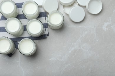 Photo of Tasty yogurt in glass jars on light grey marble table, flat lay. Space for text