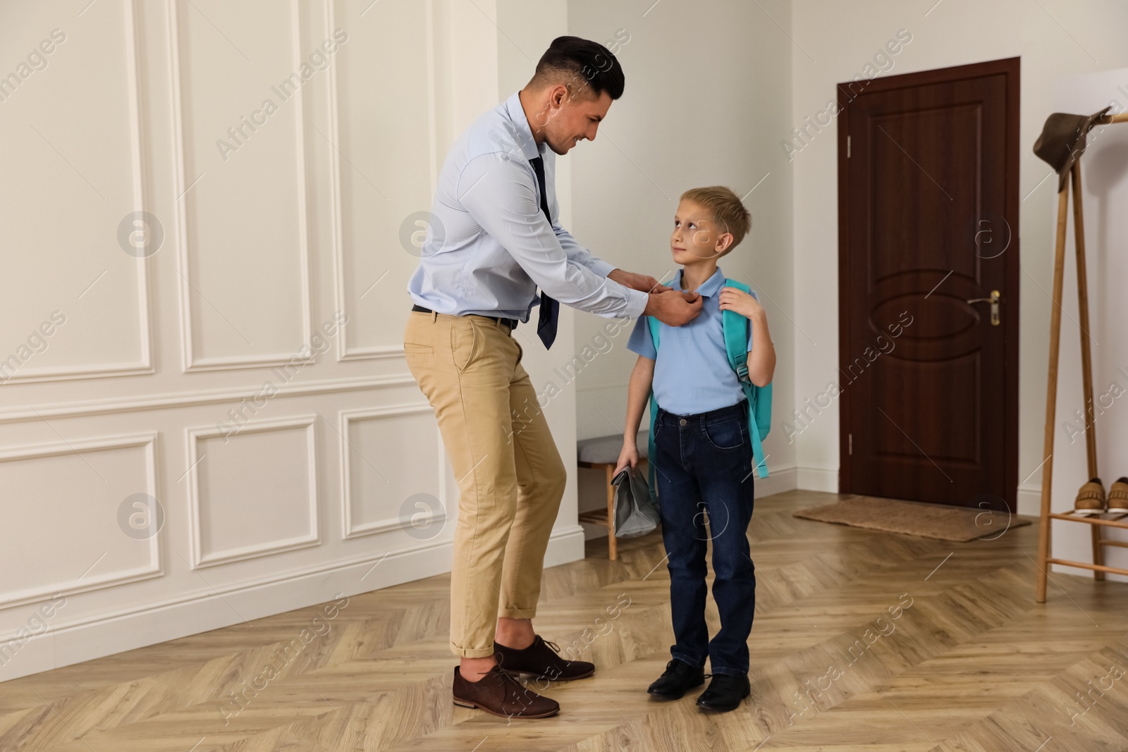 Photo of Father helping his little child get ready for school in hallway