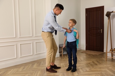 Photo of Father helping his little child get ready for school in hallway
