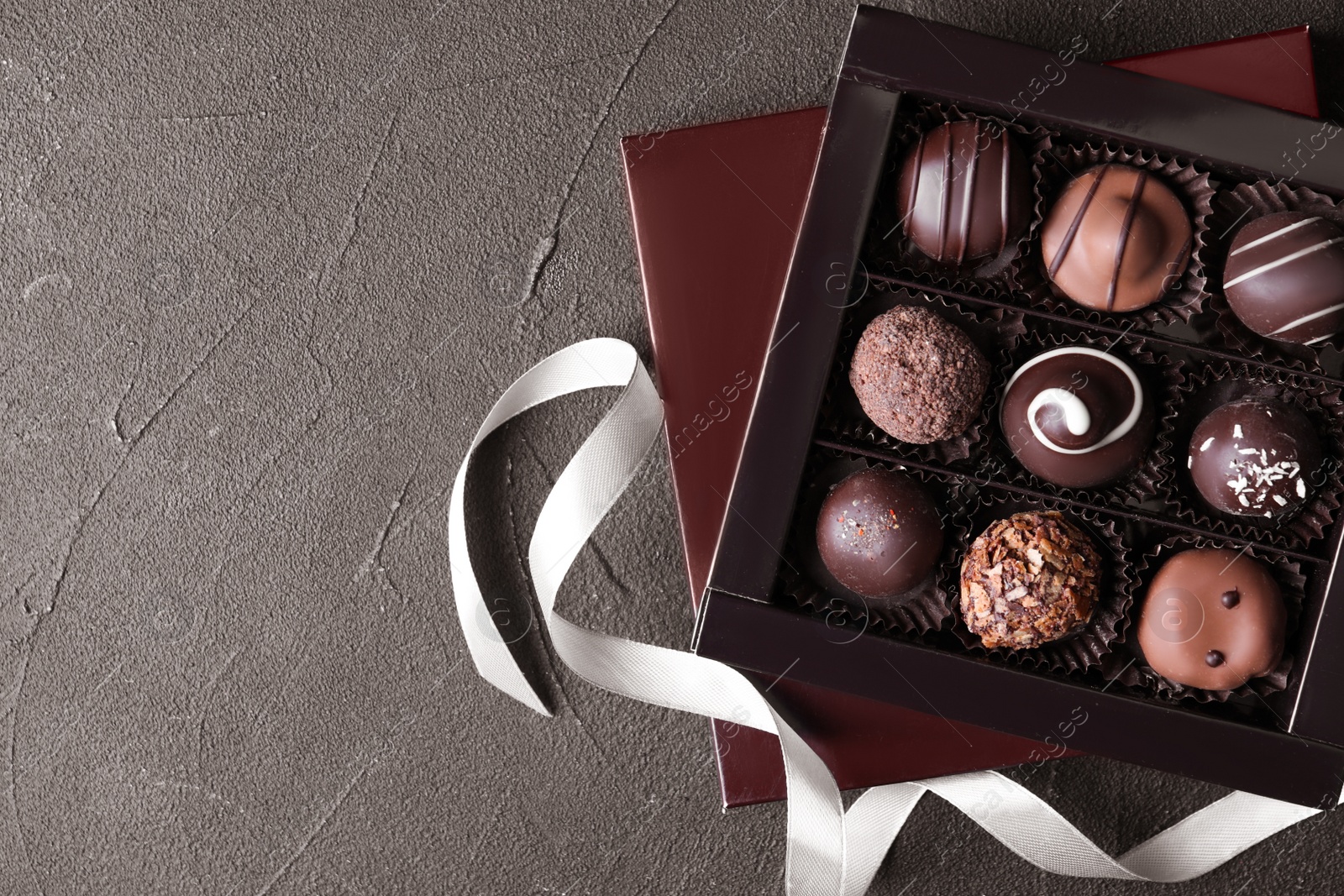 Photo of Box with tasty chocolate candies on black table, flat lay