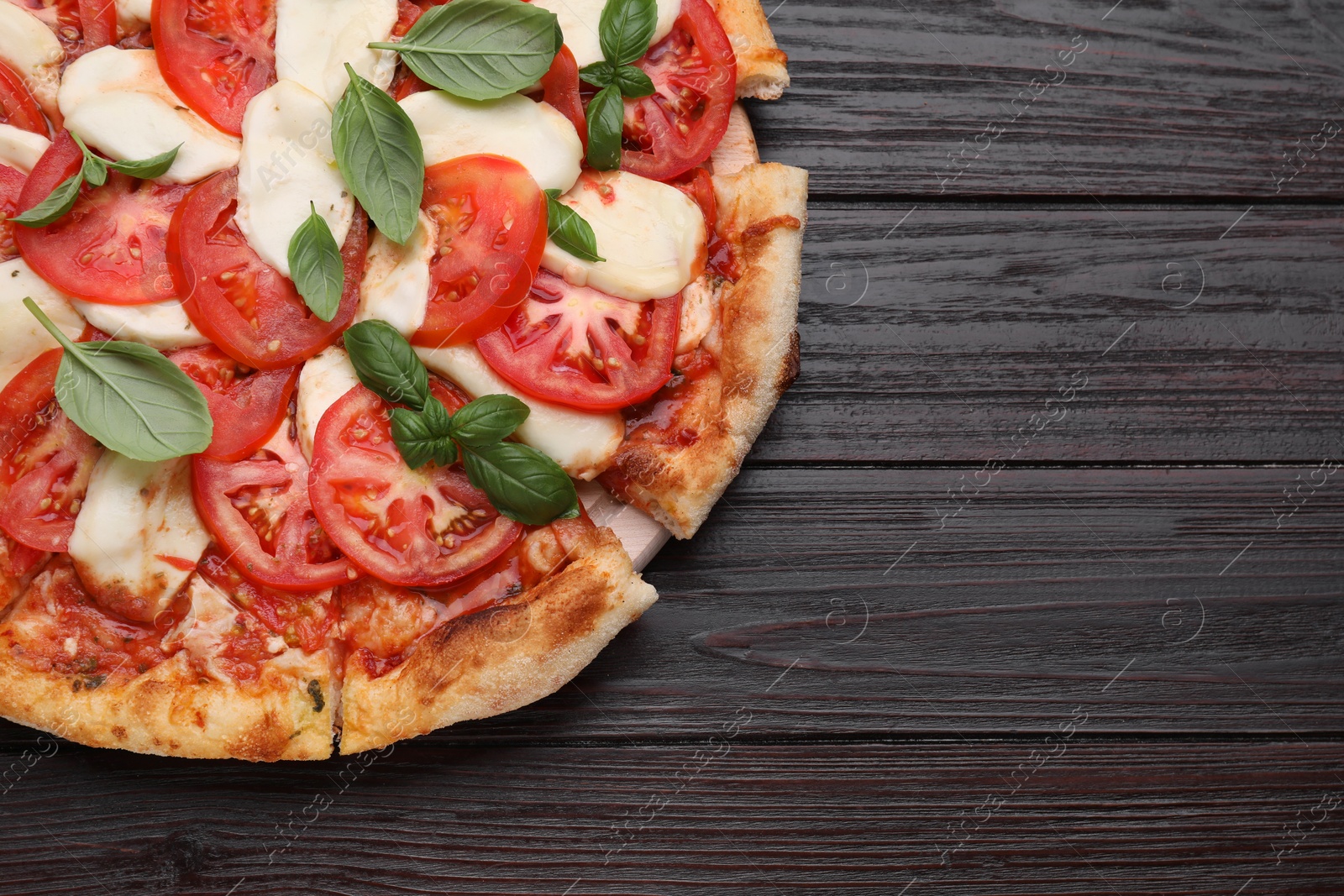 Photo of Delicious Caprese pizza with tomatoes, mozzarella and basil on dark wooden table, top view. Space for text