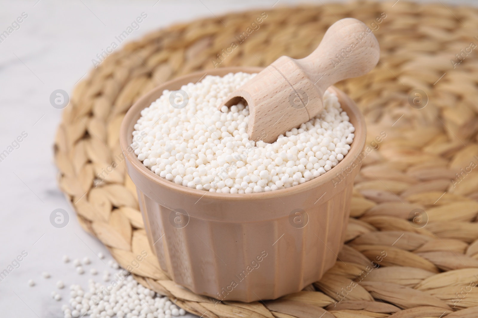 Photo of Tapioca pearls and scoop in bowl on wicker mat, closeup