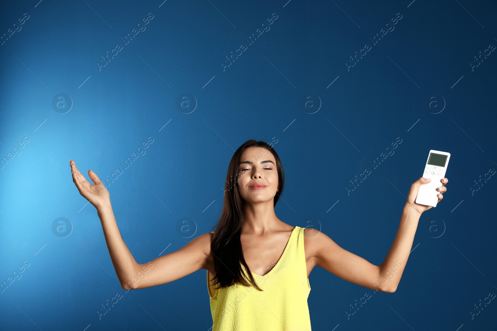 Photo of Young woman with air conditioner remote on blue background