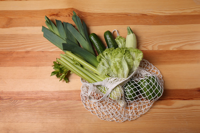 Photo of White net bag with vegetables on wooden background, top view