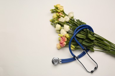 Photo of Stethoscope and flowers on white background, flat lay with space for text. Happy Doctor's Day