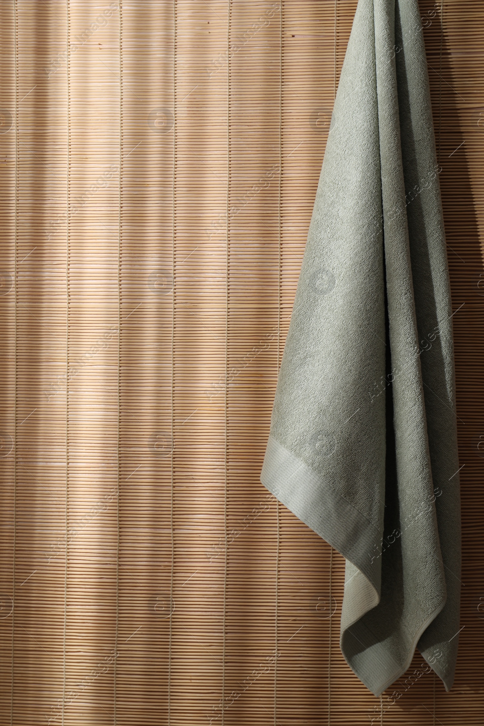 Photo of Soft towel hanging on bamboo wall indoors, space for text