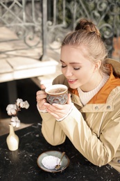 Photo of Young woman enjoying tasty coffee at table outdoors