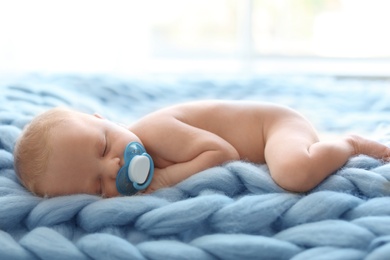 Adorable newborn baby lying on knitted blanket indoors