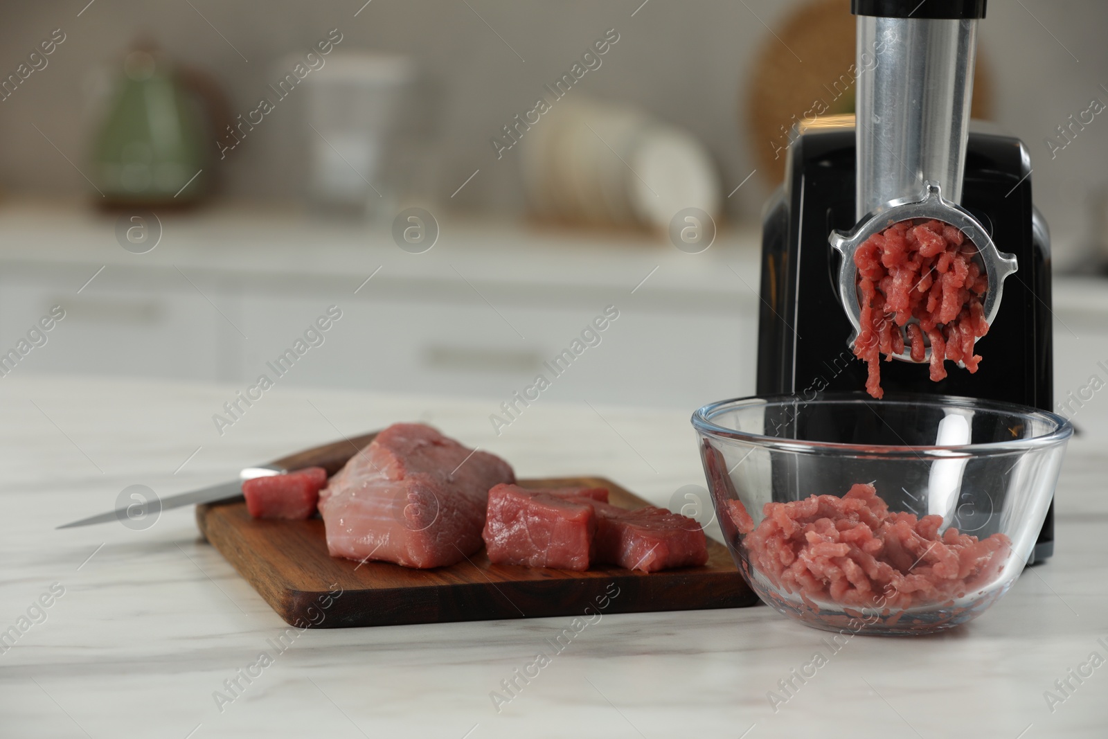 Photo of Electric meat grinder with beef mince on white table in kitchen