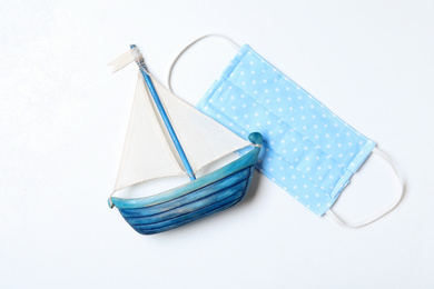 Photo of Homemade protective mask and toy sailboat on white background, flat lay. Sewing for child