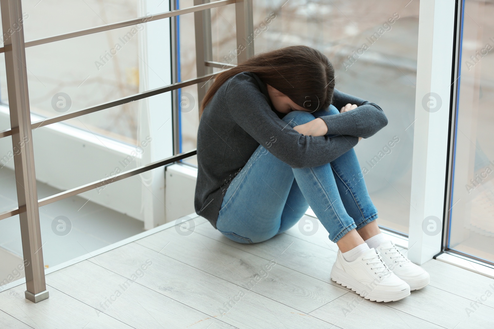 Photo of Upset teenage girl sitting at window indoors