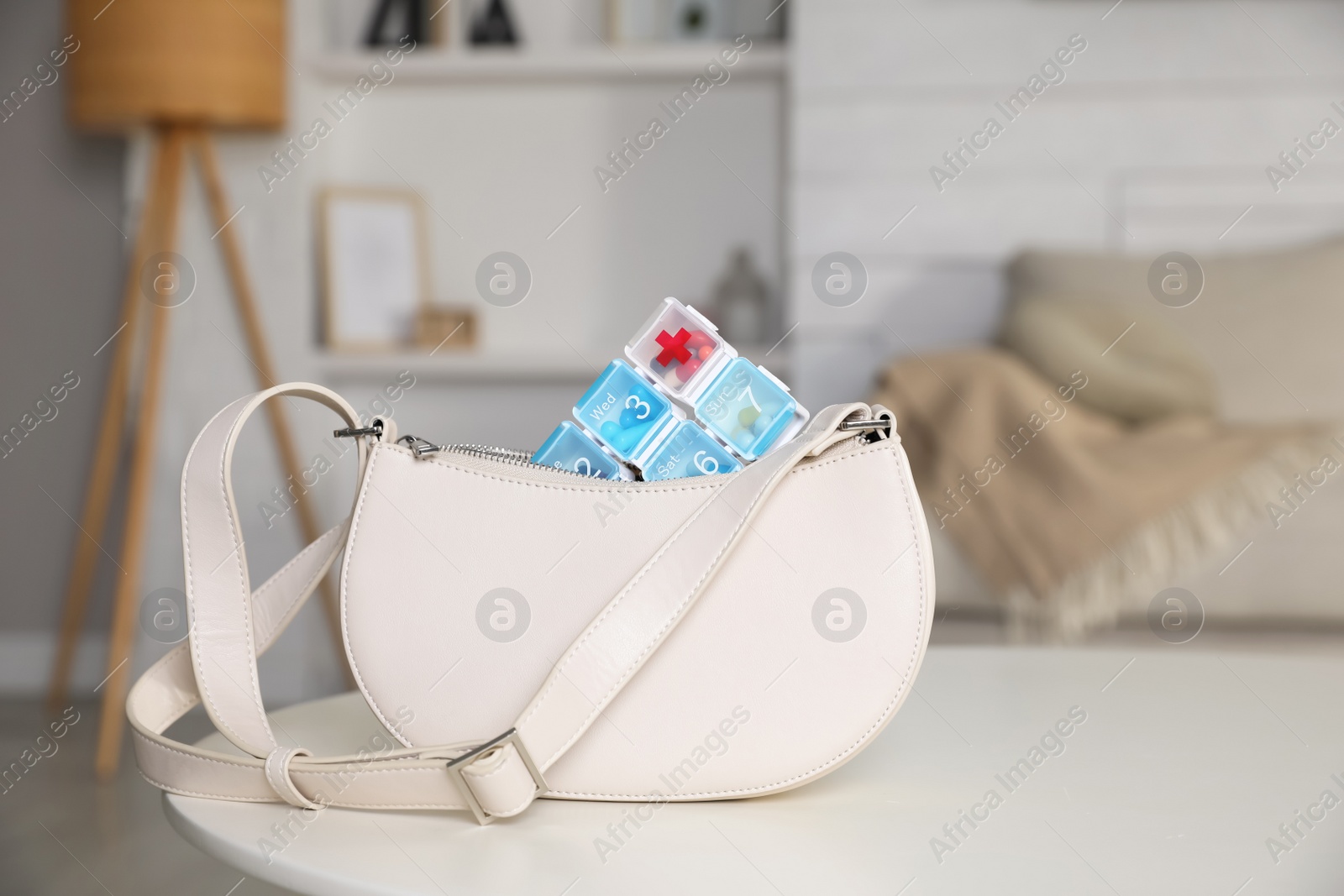 Photo of Stylish women's bag with plastic pill box on white table in room. Space for text