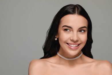 Young woman wearing elegant pearl jewelry on grey background, space for text