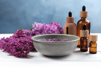 Photo of Cosmetic products and lilac flowers on white wooden table