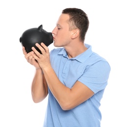 Young man kissing piggy bank on white background