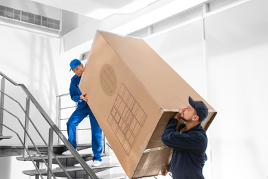 Professional workers carrying refrigerator on stairs indoors