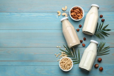 Photo of Different organic vegan milks and nuts on light blue wooden table, flat lay. Space for text