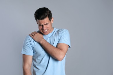 Photo of Man suffering from shoulder pain on grey background. Space for text