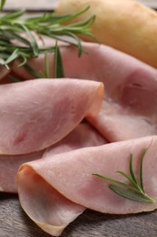 Photo of Slices of delicious ham and rosemary on wooden table, closeup